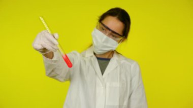 Beyaz elbiseli kadın, koruyucu maske test tüpünün içindekileri inceliyor.