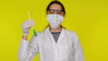 Beyaz elbiseli, koruyucu maskeli genç bir kadın test tüpüyle oynuyor.