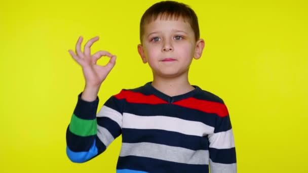 Serio niño pequeño levanta la mano y muestra bien en un fondo amarillo — Vídeos de Stock