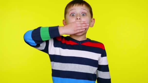 Malý chlapec je překvapen, zavírá ústa s dlaní na žlutém pozadí — Stock video