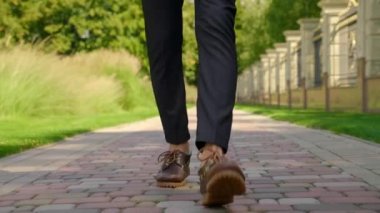 Ayakkabılı adam bacakları, pantolonu kaldırım kenarındaki parkta yürüyor.