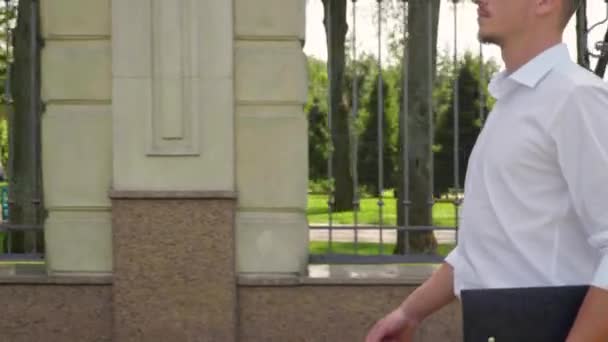 Zakenman met een laptop in de hand loopt door het park — Stockvideo