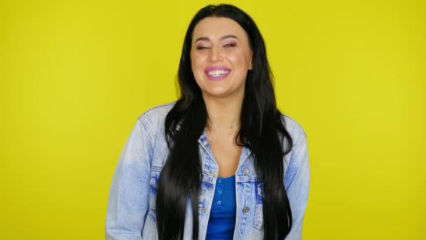 Mulher ri e olha para a câmera em um fundo amarelo com espaço de cópia — Vídeo de Stock
