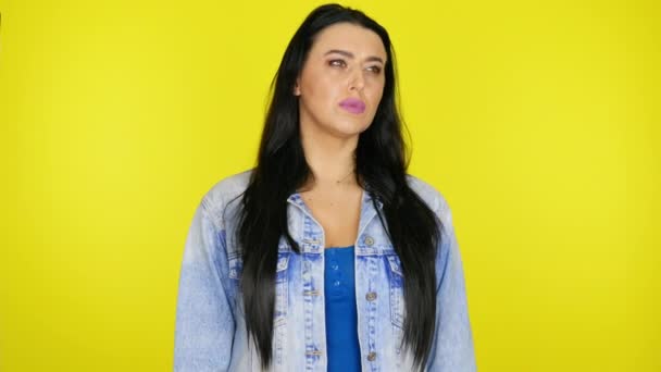 Serieuze vrouw kijkt om zich heen en denkt wat te kiezen op een gele achtergrond — Stockvideo