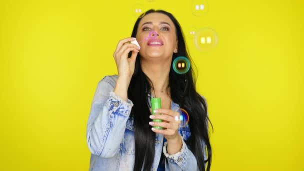 Kobieta dmucha bańki mydlane i uśmiecha się na żółtym tle z miejsca kopiowania — Wideo stockowe
