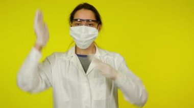 Sarı arka planda koruyucu maskeli genç bayan dans ediyor.
