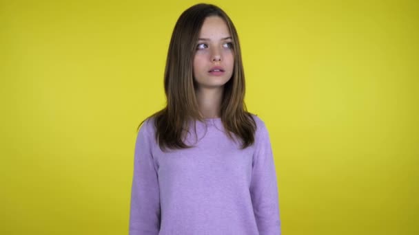 Tiener meisje kijkt rond en denkt wat te kiezen op een gele achtergrond — Stockvideo