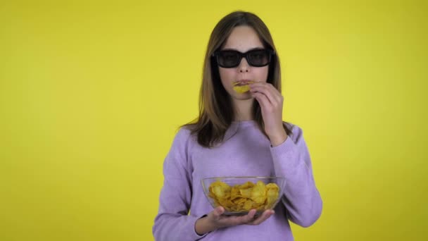 Meisje kijkt film in zwart 3D bril en eet chips van glas kom — Stockvideo