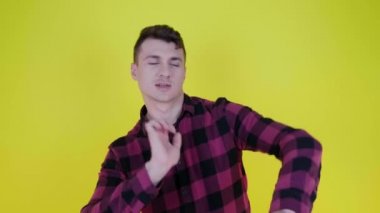 Pembe ekose gömlekli neşeli adam sarı arka planda dans ediyor ve gülümsüyor.