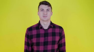 Pembe ekose gömlekli kızgın adam sarı arka planda kameraya doğru bağırıyor.