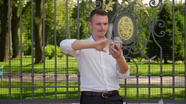 Un joven empresario esparce dólares en un parque. Imágenes 4K — Vídeos de Stock