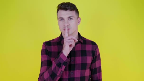 Silencio. Hombre de camisa a cuadros rosa pone dedo índice a los labios sobre fondo amarillo — Vídeos de Stock