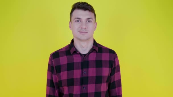 Bello giovane flirta con un occhio ammiccante e sorride su uno sfondo giallo — Video Stock