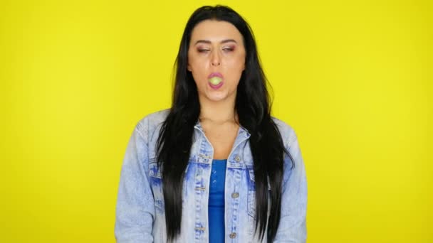 Kvinna pumpar tuggummi sedan spränger en bubbla på en gul bakgrund med kopieringsutrymme — Stockvideo