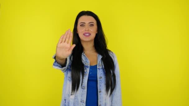 Serious woman raised hand and palm to the camera says stop on yellow background — Stock Video