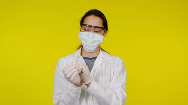 Tıbbi maskeli ve güvenlik gözlüklü genç doktor ellerine lateks eldiven takıyor.