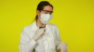 Sarı arka planda koruyucu maskeli genç bayan dans ediyor.