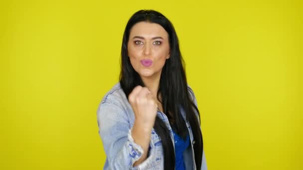 Vrouw toont een vuist op de camera op een gele achtergrond met kopieerruimte — Stockvideo