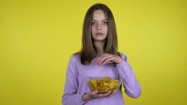 Tiener meisje eet aardappel chips met glazen kom op gele achtergrond — Stockvideo