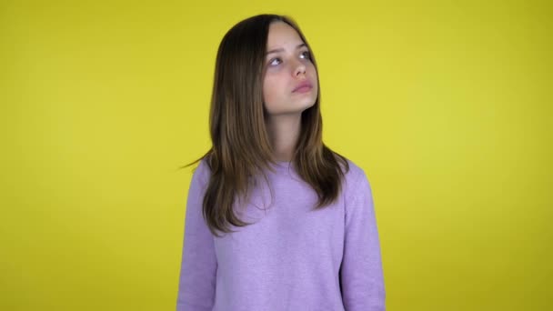 Adolescente chica mira a su alrededor y piensa qué elegir en un fondo amarillo — Vídeos de Stock