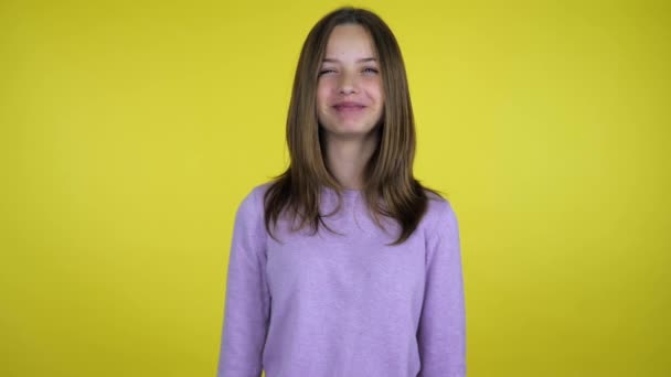 Tiener meisje in een roze trui lacht en kijkt naar de camera op gele achtergrond — Stockvideo