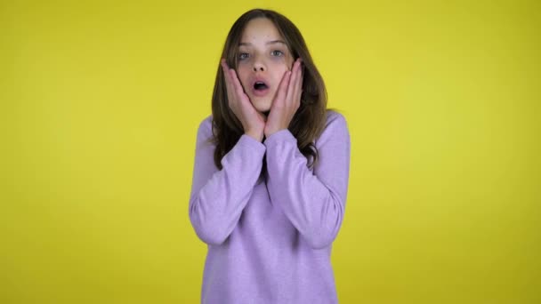 Tiener meisje heft hoofd en geschokt zet handpalmen op wangen op een gele achtergrond — Stockvideo