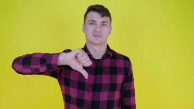 Pembe ekose gömlekli adam elini kaldırır ve sarı arka planda hoşlanmadığını gösterir.