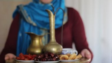 Hijab giyen Müslüman kadın. Arapça yiyecek ve içecek. Tatlı tarihleri ve siyah çay kase ile dolu bir tepsi