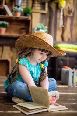  kovboy şapkalı küçük güzel kız katta oturur ve Paskalya süsleri arka plan üzerinde kitap okur
