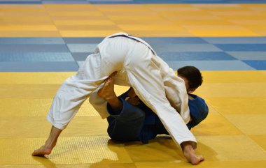 İki kimonolu judoka tatamide yarışıyor.