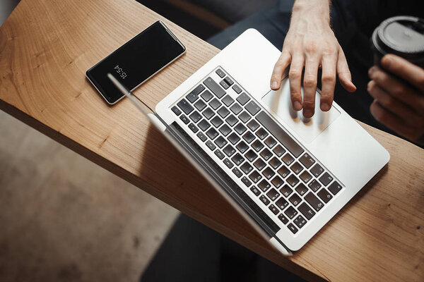 Young man is working on laptop and drinking coffee from black cup