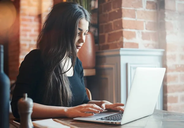 Fundersam ung kvinna som arbetar på laptop i café. — Stockfoto
