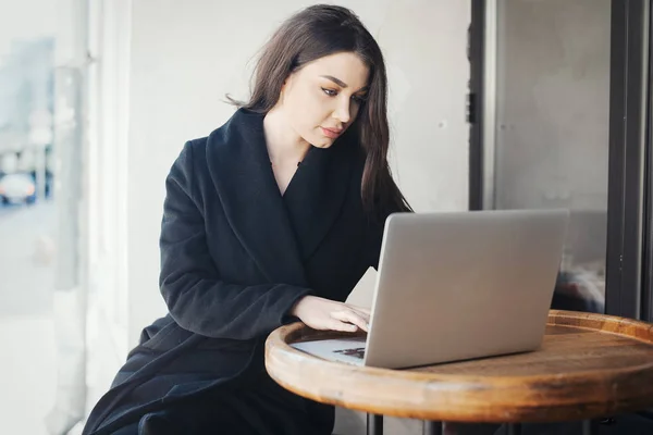 Fundersam ung kvinna som arbetar på laptop i café. — Stockfoto