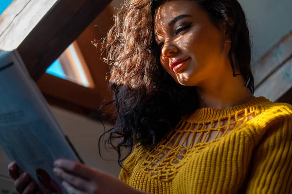 Mladá usmívající se žena v žluté útulné svetr čtení časopis v podkroví Retro Mansard a těší víkendové ráno — Stock fotografie