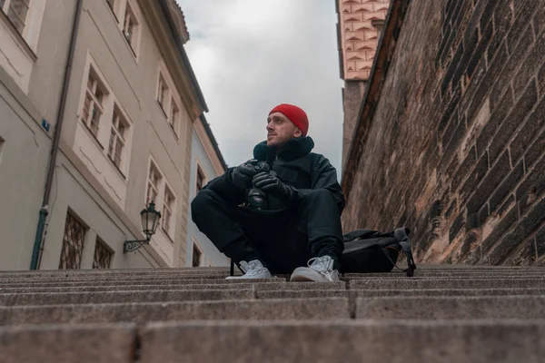 Atrakcyjny mężczyzna siedzący na schodach w centrum starego europejskiego miasta i trzymający aparat fotograficzny. Współczesny stylowy Blogger i fotograf. — Zdjęcie stockowe