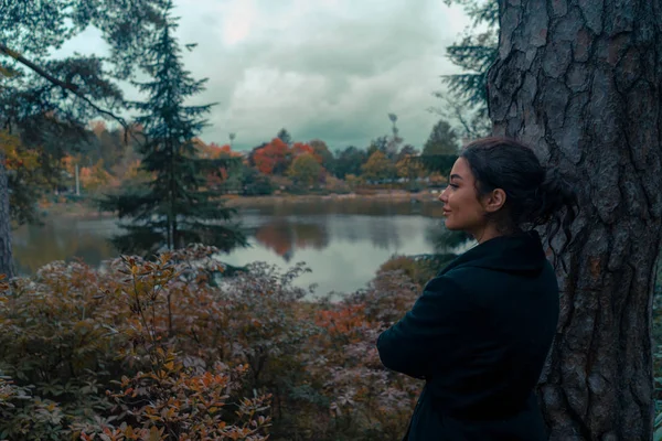 Νεαρή ελκυστική γυναίκα που κοιτάζει τη λίμνη στο όμορφο πάρκο στη Φινλανδία και χαμογελώντας. Έννοια της αρμονίας και της ενότητας με τη φύση — Φωτογραφία Αρχείου