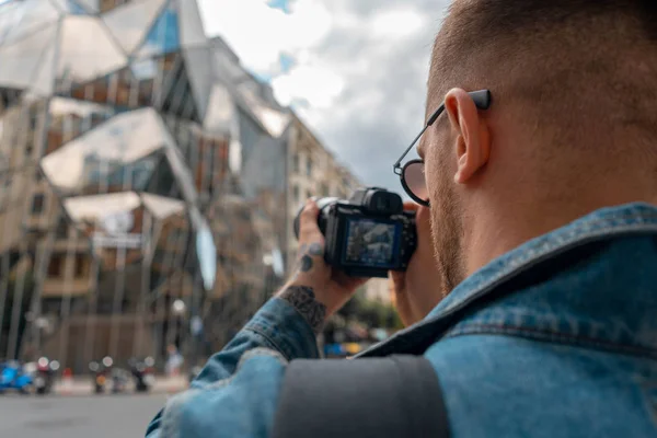 Hombre atractivo enfocando cámara fotográfica en edificio moderno. El fondo del paisaje urbano está borroso. Blogger y Traveler. Vacaciones europeas — Foto de Stock