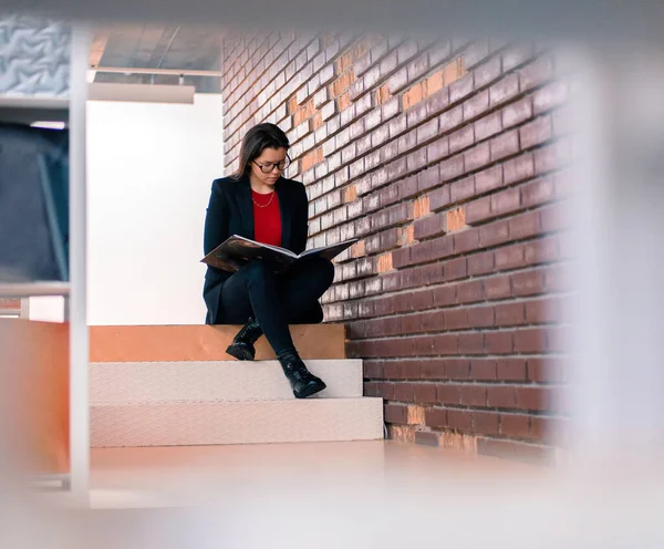 Одна жінка в сучасній бібліотеці читає книгу і сидить на сходах. Концепція інвалідів життя повне життя — стокове фото