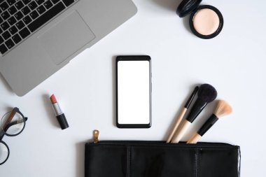 Makeup Bag With Spilling Out Cosmetic Beauty Products Near Laptop And Mobile Phone With Blank Screen. Bag Content Of Independent Woman