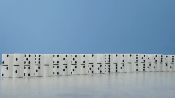 Dominoeffekt - eine Reihe von Dominosteinen, die auf blauem Hintergrund die Kette hinunterfallen — Stockvideo