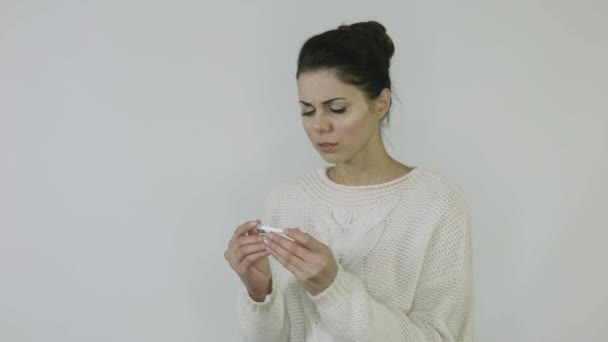 A sick girl with a cold checks the thermometer on a white background — Stock Video