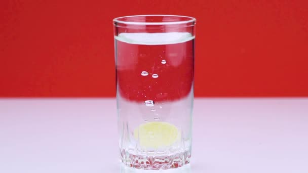 Eine Brausetablette gegen Schmerzen fällt in ein Glas und löst einen Schuss Aspirin in Zeitlupe auf rotem Hintergrund auf — Stockvideo