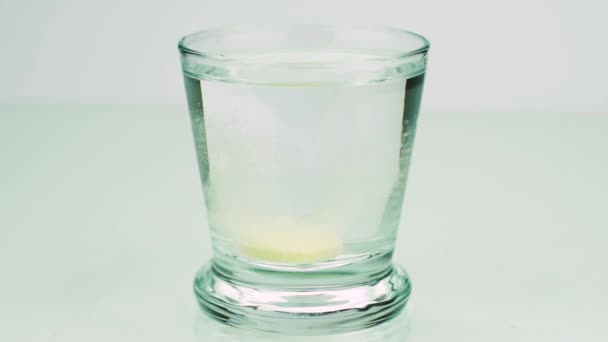 Une pilule effervescente contre la douleur tombe dans un verre et dissout l'aspiration au ralenti sur un fond coloré 