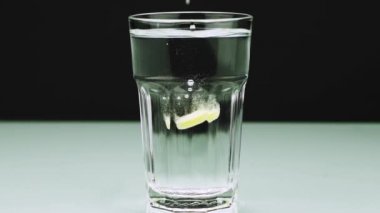 Bir efervesan hap ağrısı karşı bir cam içine düşer ve yakın çekim yavaş hareket atış aspirin renkli bir arka plan üzerinde çözülür