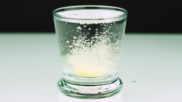 Крупным планом снимок шипучей таблетки от боли падает в стакан и растворяет замедленный укол аспирина на цветном фоне — стоковое видео