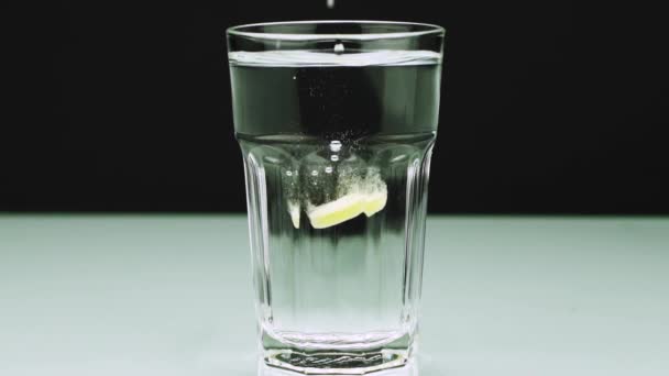 Une pilule effervescente contre la douleur tombe dans un verre et dissout Plan rapproché au ralenti de l'aspirine sur un fond coloré 