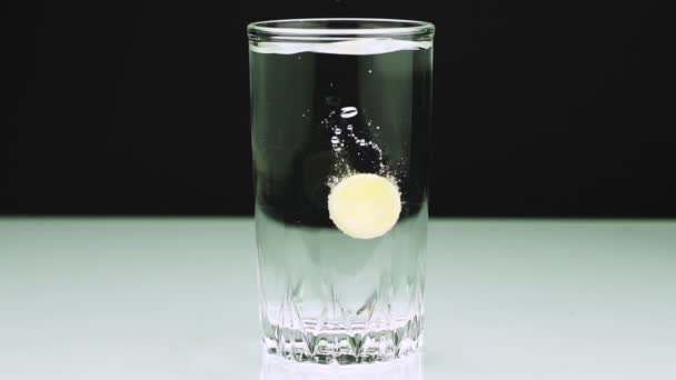 Un comprimé effervescent contre la douleur tombe dans un verre et dissout Gros plan plan plan lent de l'aspirine sur fond noir 