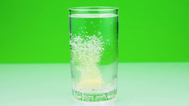 对疼痛的气泡片的特写镜头落入玻璃杯中, 在绿色背景下溶解慢动作的阿司匹林。 — 图库视频影像