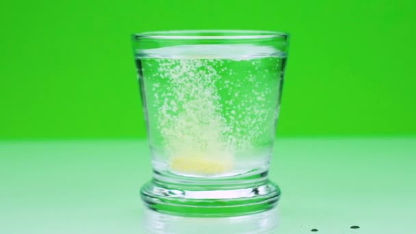 Ένα αναβράζον δισκίο κίτρινο εναντίον πόνου πέφτει σε ένα ποτήρι και διαλύει αργή κίνηση πυροβολισμό της ασπιρίνης σε πράσινο φόντο — Αρχείο Βίντεο