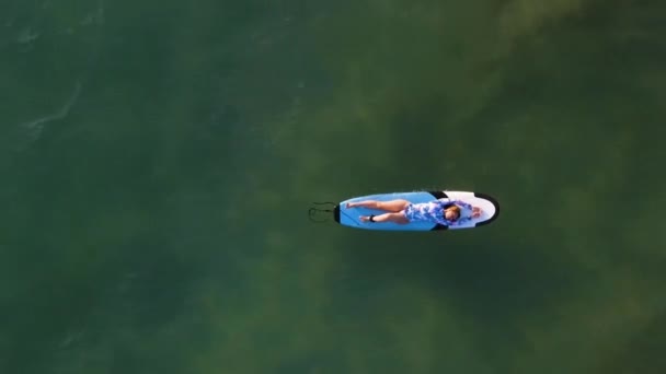 Bovenaanzicht van een meisje liggend op een surf op de golven van de Oceaan in de tropen, het zandstrand van de Atlantische Oceaan — Stockvideo